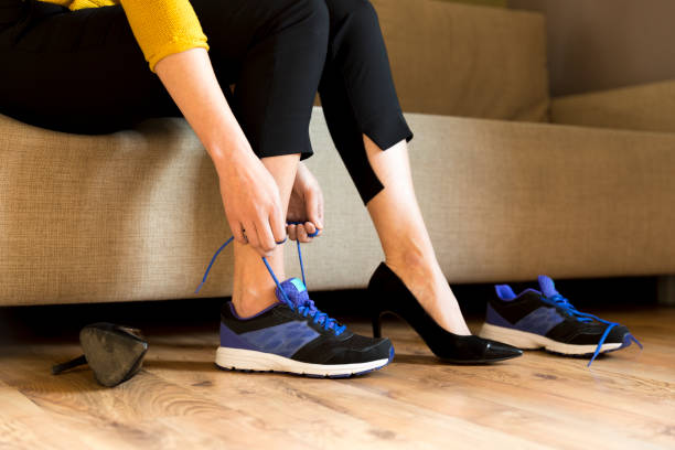 Woman changing high heels, office shoes after working day while sitting on the couch, ready to take a walk or run Woman changing high heels, office shoes after working day while sitting on the couch, ready to take a walk or run women high heels stock pictures, royalty-free photos & images