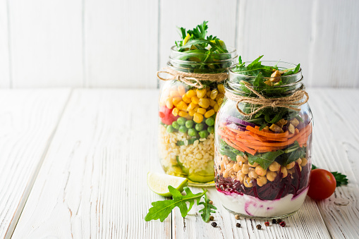 Healthy homemade salads with chickpeas, bulgur and vegetables in mason jars on white wooden background. Selective focus. Copy space.