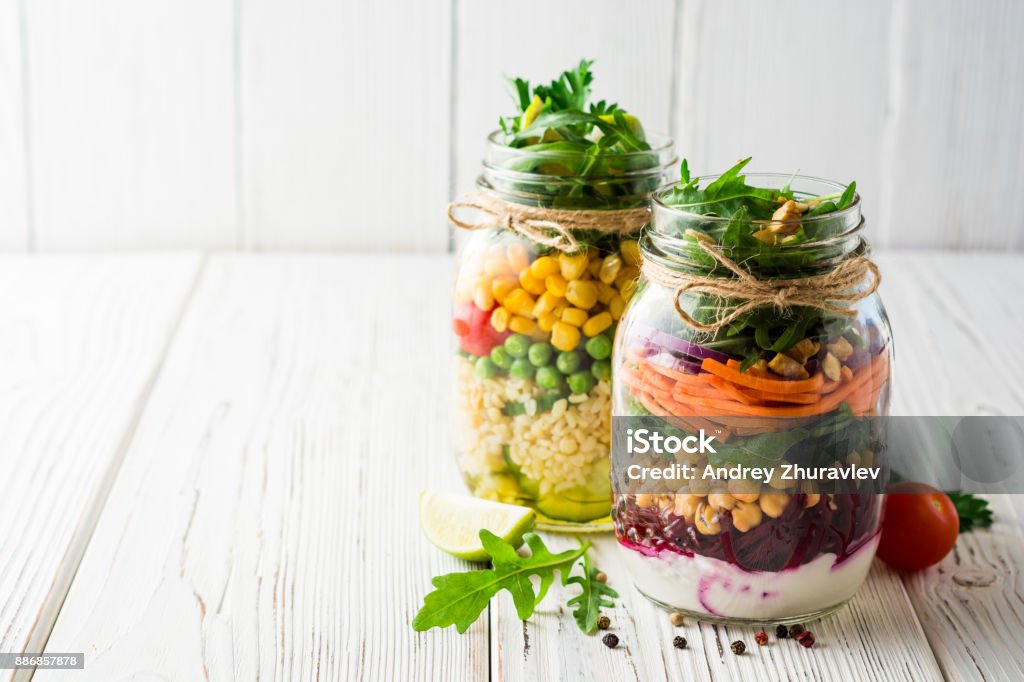 Healthy homemade salads with chickpeas, bulgur and vegetables in mason jars on white wooden background. Healthy homemade salads with chickpeas, bulgur and vegetables in mason jars on white wooden background. Selective focus. Copy space. Mason Jar Stock Photo