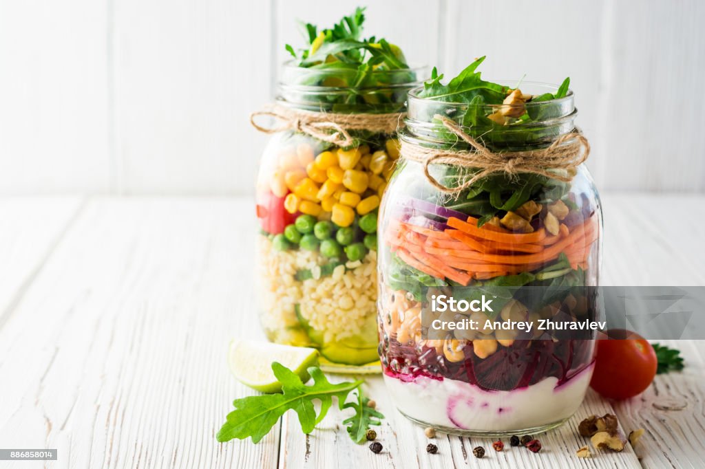 Healthy homemade salads with chickpeas, bulgur and vegetables in mason jars on white wooden background. Healthy homemade salads with chickpeas, bulgur and vegetables in mason jars on white wooden background. Selective focus. Copy space. Mason Jar Stock Photo