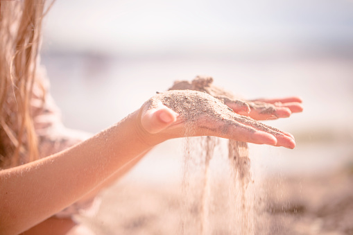 Detail of sand running through open hands. In the corner of the image, we can see the hair of the little girl who is playing with the sand.