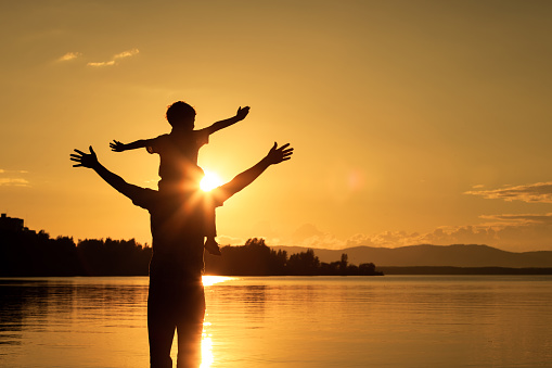 father and son playing on the coast of lake in the mountains of at the sunset time