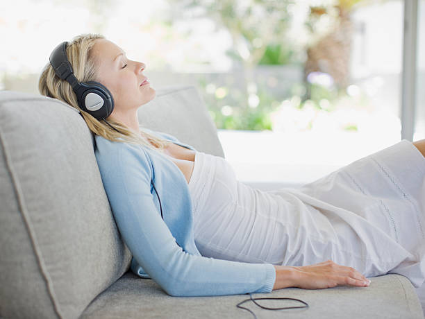 femme en écoutant des écouteurs dans la salle de séjour - lying on side audio photos et images de collection