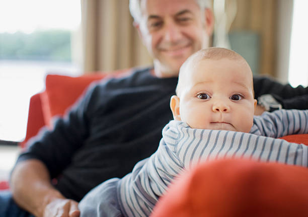 hombre jugando con bebé en sofá - abuelo y bebe fotografías e imágenes de stock