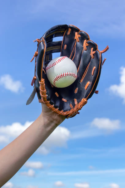 istock Arm holding baseball with glove  in blue sky 886894682