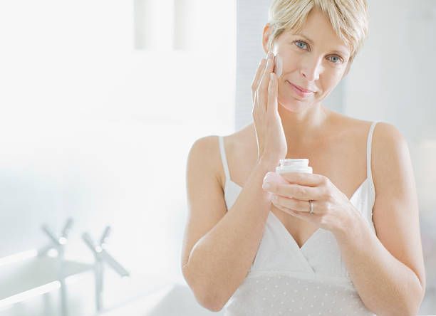 donna applicando crema viso al mattino - mettersi la crema foto e immagini stock