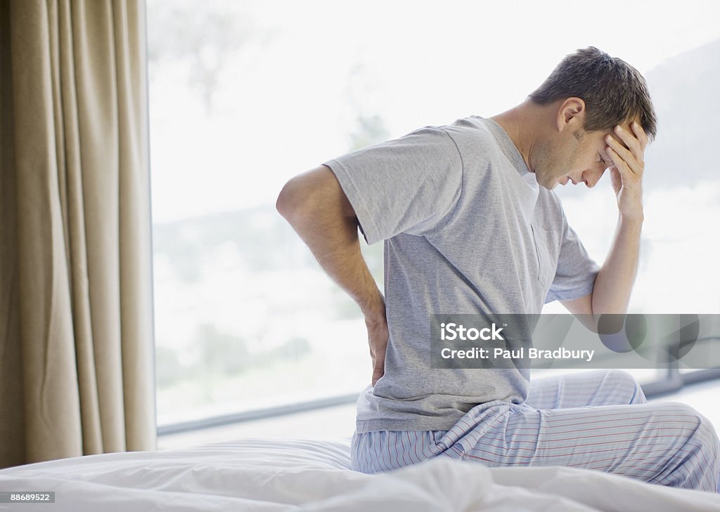 Man sitting on bed with backache and headache  Pain Stock Photo