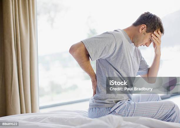 Man Sitting On Bed With Backache And Headache Stock Photo - Download Image Now - Pain, The Human Body, Backache