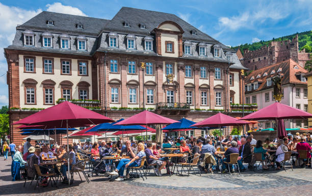 Heidelberg, Germany-May 21, 2016- Visitors, tourists and residents gather at tables under red and blue umbrellas to enjoy wine, beer and other beverages in the Kornmarkt, a market square in Heidelberg, Germany.