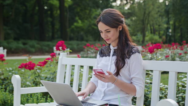 istock Lady Sitting in the Park and Using Laptop and Phone 886931108