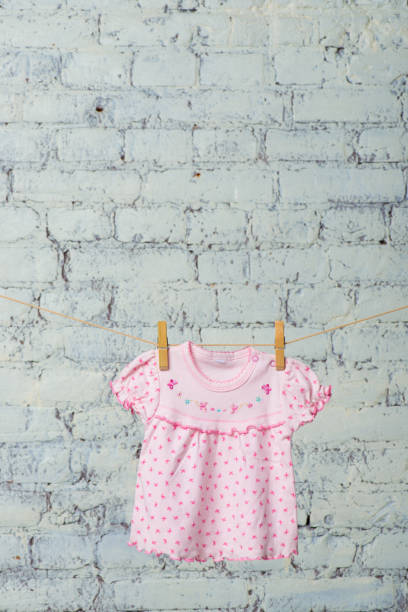 istock A baby dress dries on a rope against a white brick wall 886933536