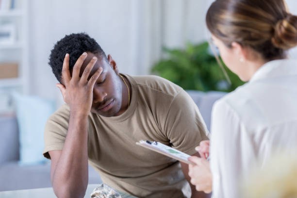 Upset soldier talks with therapist Distraught African American soldier has is head in his hands while talking with a healthcare professional. black military man stock pictures, royalty-free photos & images
