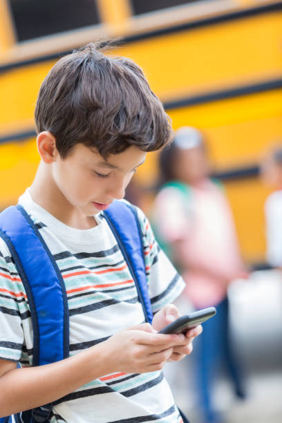 istock Schoolboy uses smart phone while waiting for bus 886933812