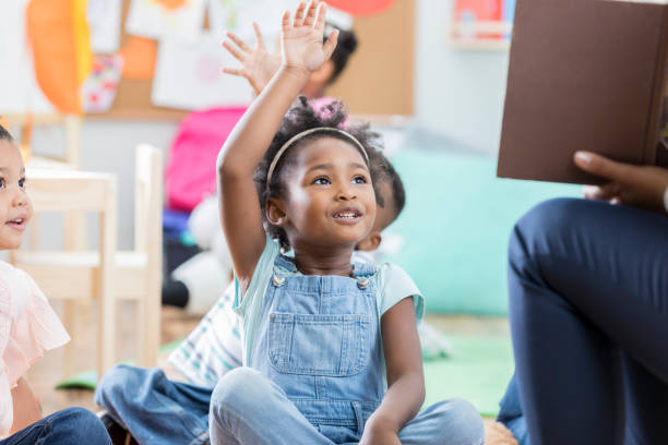 petite fille lève la main durant l’heure du conte - child classroom teacher learning photos et images de collection
