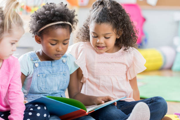 istock Three little girls read together at day care 886934236
