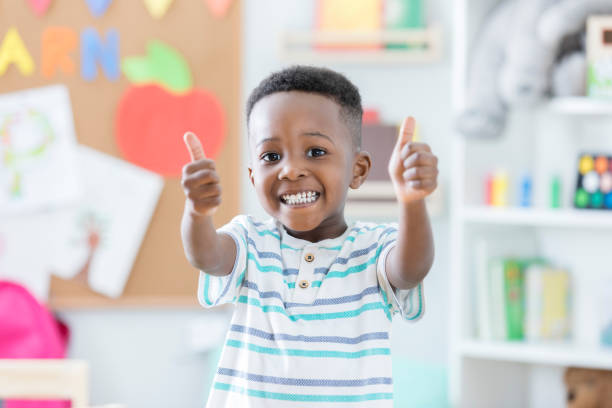 entzückende junge gibt daumen nach oben in der vorschule - cheerful studying child education stock-fotos und bilder