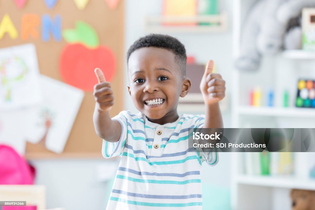 Adorable boy gives thumbs up in preschool An adorable preschool age little boy smiles for the camera as he stands in his preschool classroom and gives a thumbs up.  He loves school! Child Stock Photo
