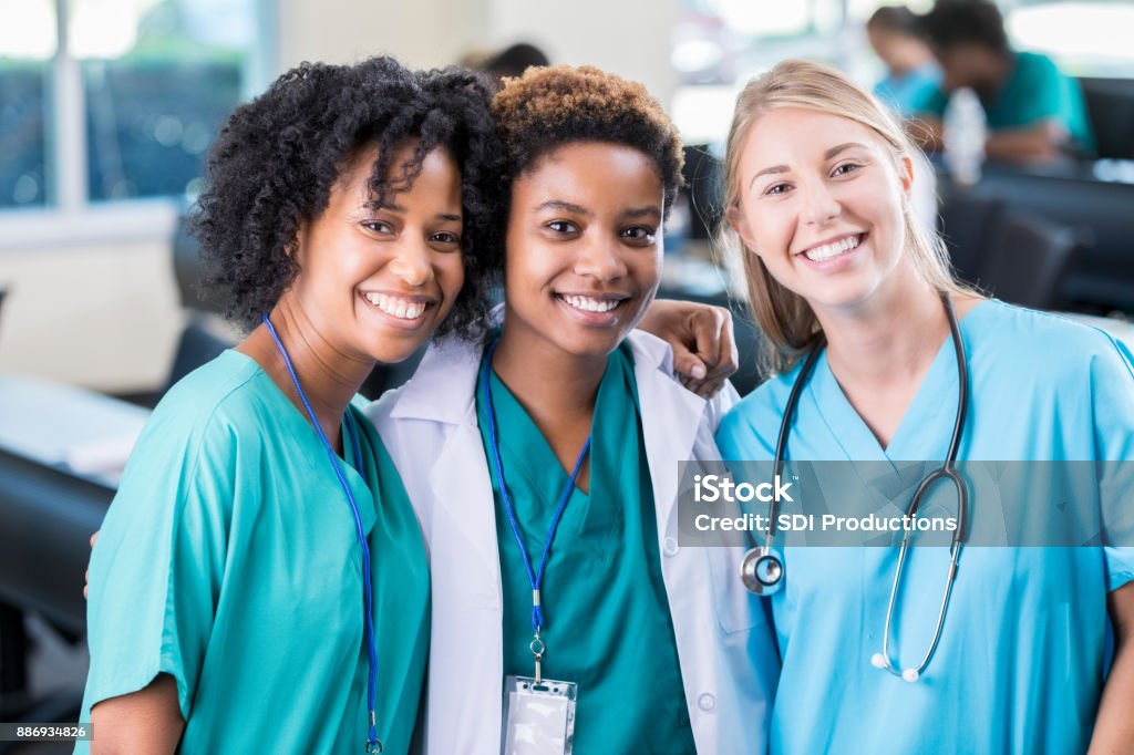 Confident medical school friends Diverse female medical school friends after class. They are smiling at the camera. They are wearing scrubs and lab coats. Nurse Stock Photo