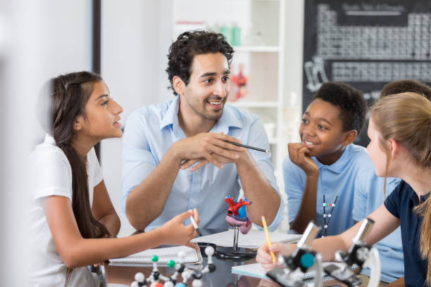 istock Friendly teacher engages students during biology lab 886935000