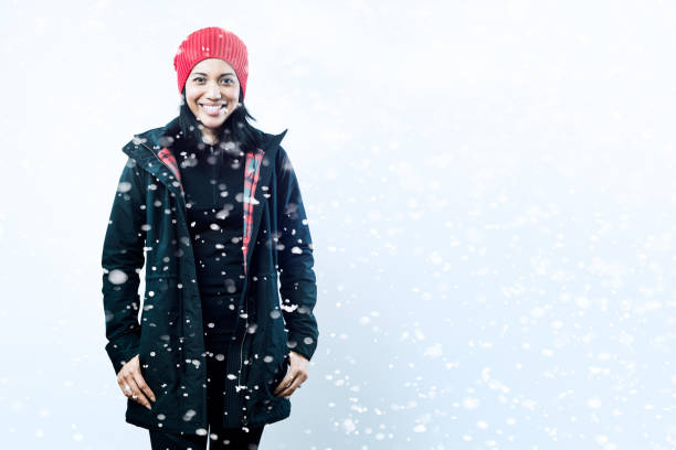 A happy Asian - Pacific Island woman stand in a light snowfall outdoors, a big smile on her face.  Horizontal with copy space.