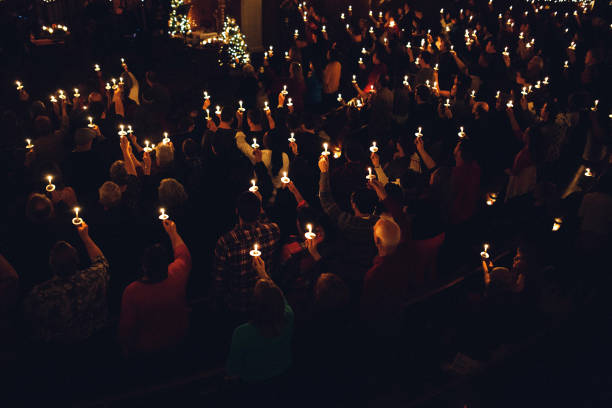 A large group of people in a church congregation hold lighted candles aloft during a time of celebration on the eve of Christmas day, the final day of advent.