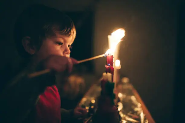 A cute little boy lights a row of candles for the Advent season, a time of remembrance and reflection on the coming birth of Jesus Christ and the Christmas season.