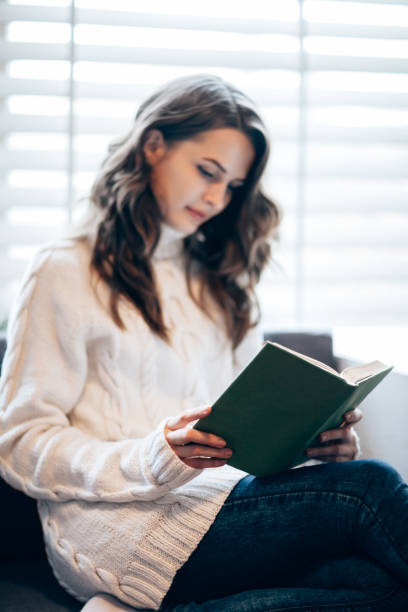 istock Young beautiful woman reading book at home 886949098