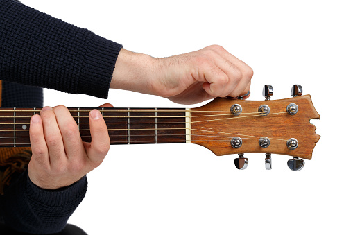 Men's hands in a black sweater that tunes the sound of a six-stringed guitar. Isolated on white background.