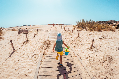 Photo of a little boy holding his sand bucket during his walk on a boardwalk that leads to the beach