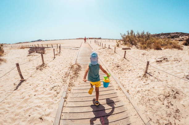 On my way to the beach Photo of a little boy holding his sand bucket during his walk on a boardwalk that leads to the beach bucket photos stock pictures, royalty-free photos & images
