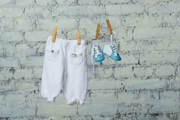 Children's shoes and pantyhose dry on a rope against a white brick wall