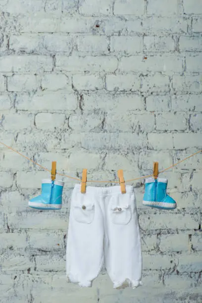 Children's boots and pantyhose dry on a rope against a white brick wall