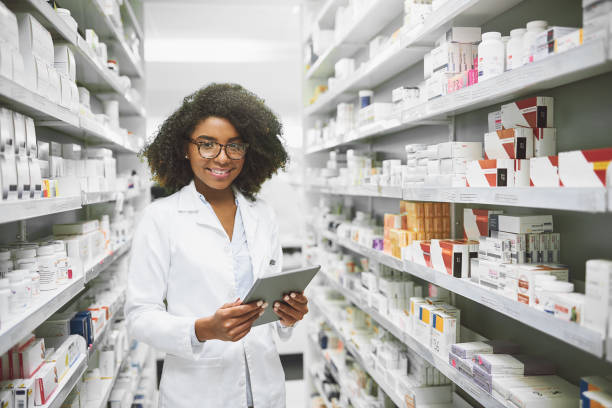 We have all the medication anybody would ever need Portrait of a cheerful young female pharmacist standing with a digital tablet while looking at the camera in a pharmacy chemist photos stock pictures, royalty-free photos & images