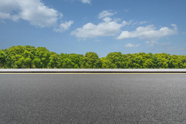 アスファルトの道路と青空の下で緑の木々 - 横から見た図 ストックフォトと画像