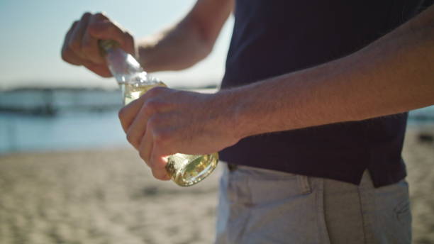 istock Young Man on the Beach Opening a Bottle 887021294