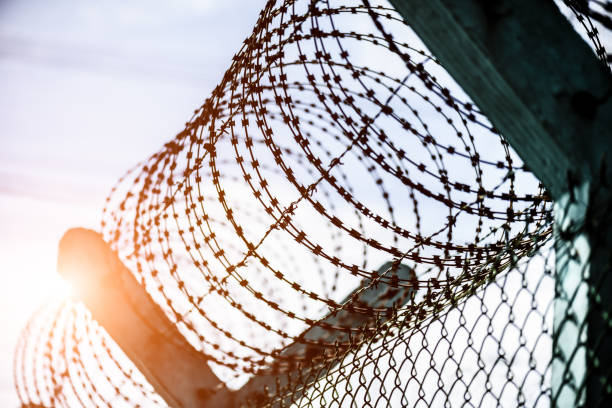 istock Closeup a security fence with barbed wire. Human Rights and social justice abstract concept. 887028690
