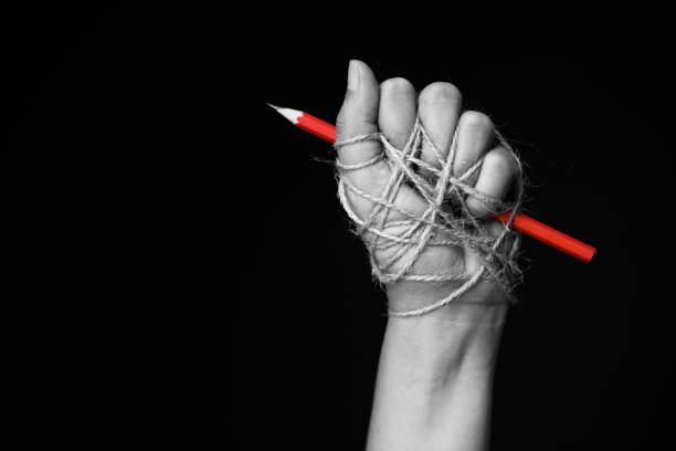 Hand with red pencil tied with rope, depicting the idea of freedom of the press or freedom of expression on dark background in low key. international human rights day concept. Hand with red pencil tied with rope, depicting the idea of freedom of the press or freedom of expression on dark background in low key. international human rights day concept. censorship photos stock pictures, royalty-free photos & images