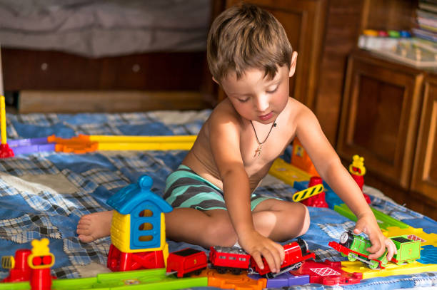 istock Little blond kid boy is playing with plastic trains and railway indoor. 887032066