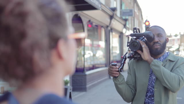 Man with video camera videoing woman talking on urban sidewalk