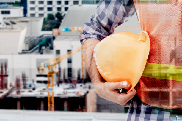 istock Engineer holding in hand yellow helmet on construction background - Double exposure photo 887133546