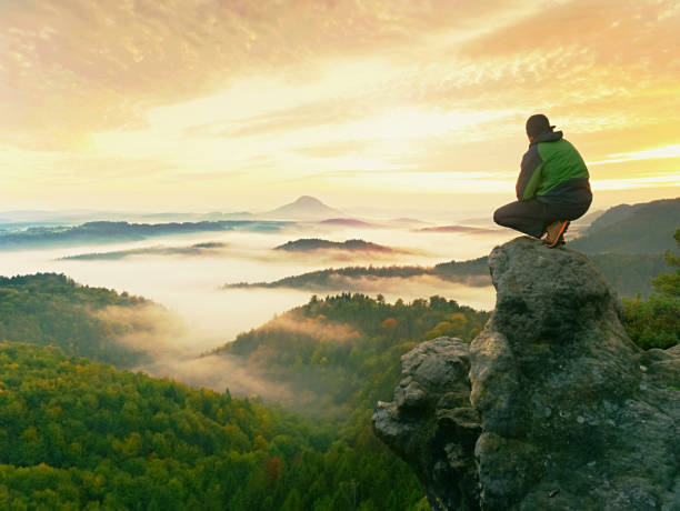 istock Hiker man take a rest on mountain peak. Man sit on sharp summit and enjoy spectacular view. 887154434