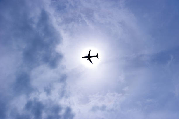 Flying aircraft at daytime silhouette through sun with circular sunlight and cloudy sky