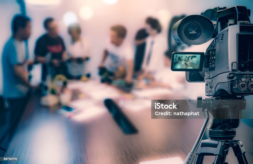 Videocamera che scatta lo streaming video in diretta presso persone che lavorano in background - Foto stock royalty-free di Videocamera