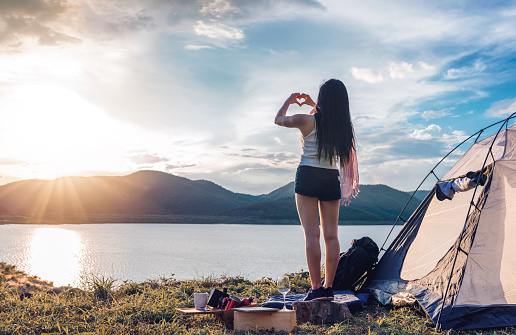 young woman make hands in heart shape show up to the sky and enjoy view of magnificent landscape while tenting on vacation.