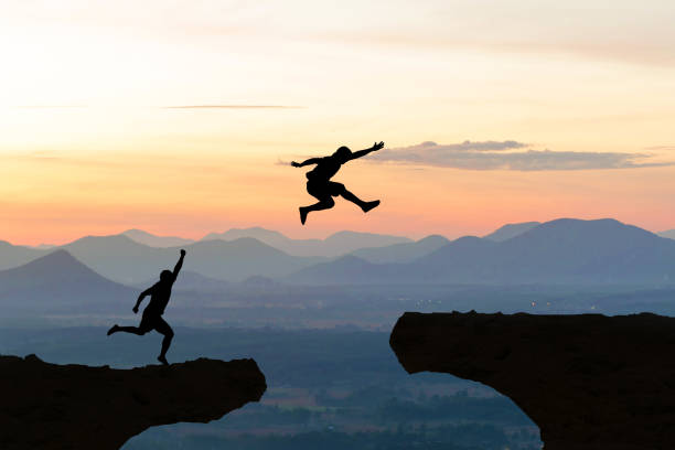 istock Men jump cliff sun light over silhouette 887194970