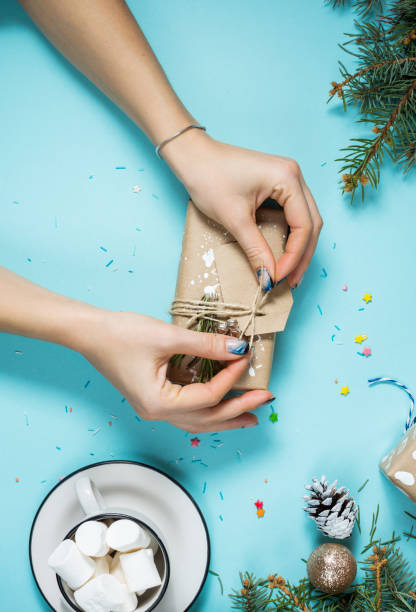 istock Female hands wrapping christmas gift box above blue table. Top view 887209528
