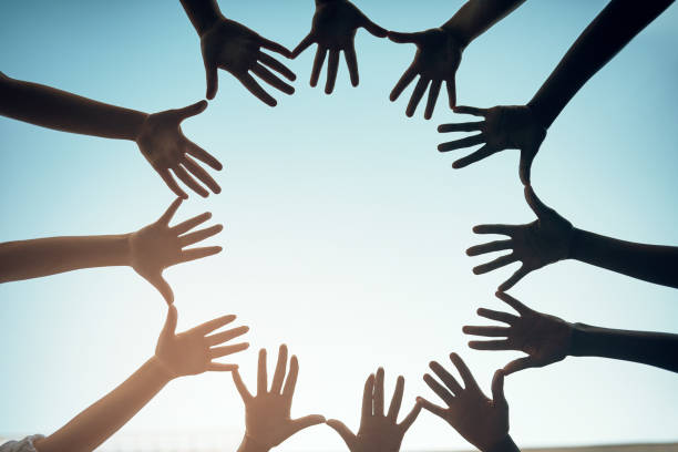 Low angle shot of a group of unidentifiable people forming a circle with their hands against a bright blue sky
