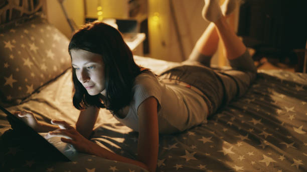 istock Attractive smiling woman relaxing on the bed using tablet computer at night at home 887242712