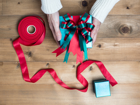 Creative hobby. Woman's hands wrap christmas holiday handmade present in craft paper with twine ribbon. Making bow gift box, decorated with cute object on wooden table, top view.flat lay composition