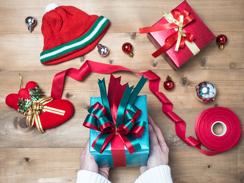 Creative hobby. Woman's hands wrap christmas holiday handmade present in craft paper with twine ribbon. Making bow gift box, decorated with cute object on wooden table, top view.flat lay composition